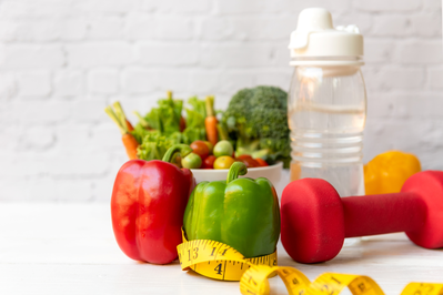 assorted vegetables, water bottle, measuring tape, and dumbbell to represent diet and exercise