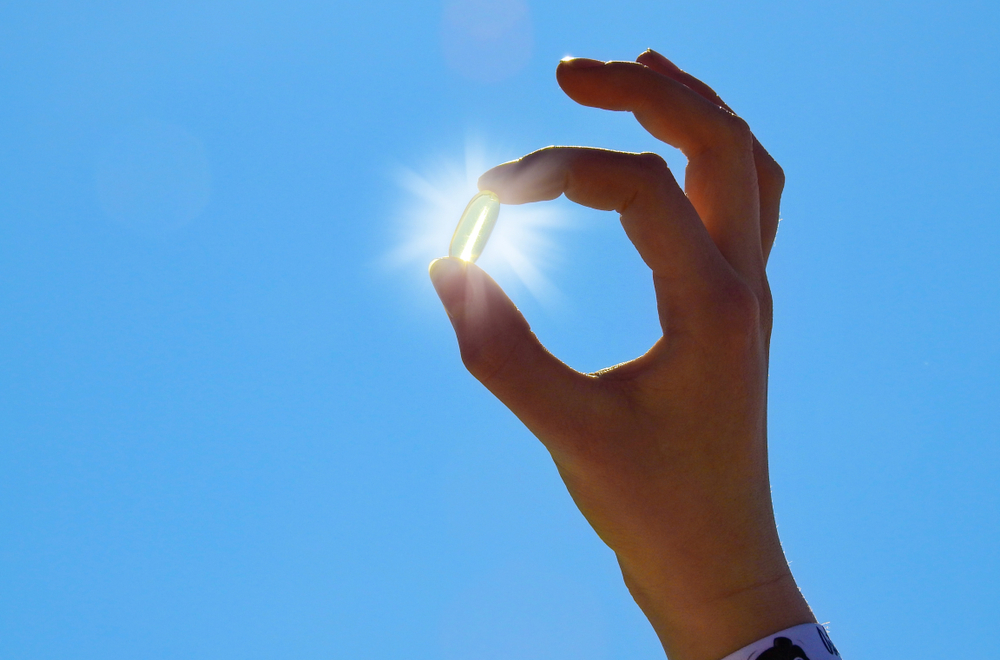 hand holding vitamin D supplement against the sun in a blue sky